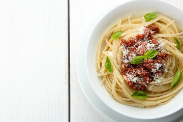 Spaghetti Bolognese with parmesan cheese in white bowl, on color wooden background
