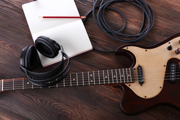 Fototapeta na wymiar Electric guitar with headphones and notebook on wooden table close up