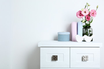 Beautiful flowers in vase with books on wall background