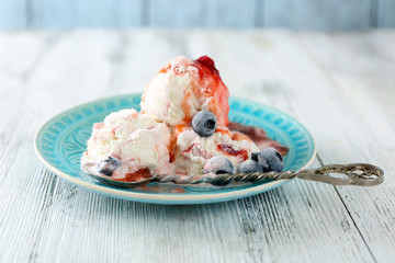 Delicious ice cream with fresh frozen berries and sauce, on color wooden background