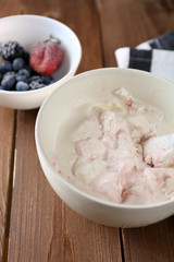 Delicious vanilla ice cream in bowl and frozen berries, on wooden background