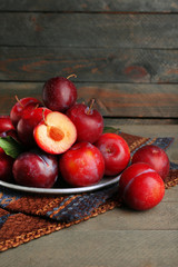 Ripe plums in metal plate on wooden background