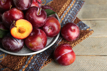 Ripe plums in metal plate on wooden table, closeup