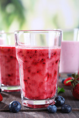 Glasses of berry smoothie on wooden table on blurred background