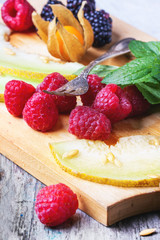 Berries, mint and melon on wooden cutting board