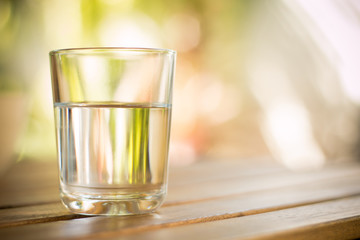glass of water on wooden table bokeh background - vintage style picture