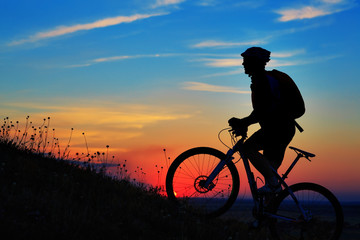 Silhouette of a biker and bicycle on sky background.