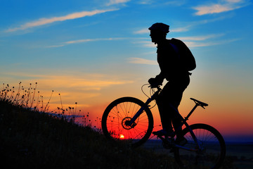 Naklejka na ściany i meble Silhouette of a biker and bicycle on sky background.