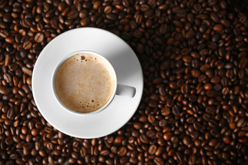 Cup of coffee with foam over grains, top view