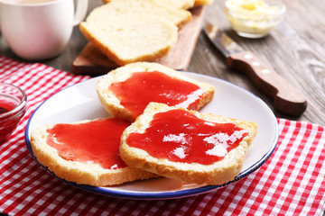Bread with butter and homemade jam in white plate on red checkered napkin, closeup