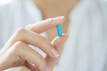 Hand holding blue capsule pill
