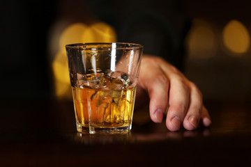 Whiskey glass tumbler in male hand on bar counter