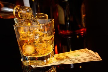barman pouring whiskey in front of whisky glass and bottles near dollars