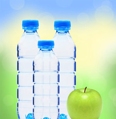 Blue bottles with water and green apple over blurred nature back