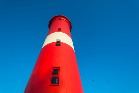 Shipping Lighthouse red and white markings against blue morning sky