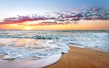 Kleurrijke oceaanstrandzonsopgang met diepblauwe hemel en zonnestralen.