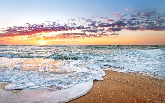 Fototapeta Colorful ocean beach sunrise with deep blue sky and sun rays.