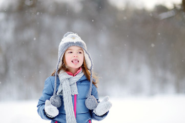 Fototapeta na wymiar Funny little girl catching snowflakes in winter park