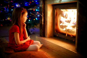 Happy little girl sitting by a fireplace on Christmas eve