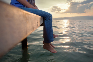 Low section of two people enjoing sunset while sitting on the pier with their feet above water - Powered by Adobe