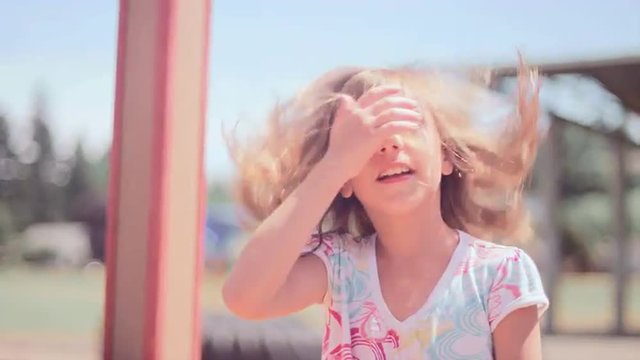 A girl hangs upside down from monkey bars and then jumps down and smiles

