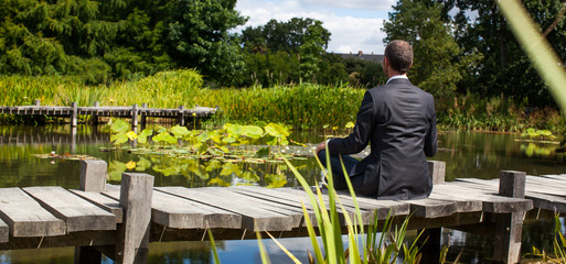 corporate green break - meditating middle age male professional sitting on a wooden bridge in the...