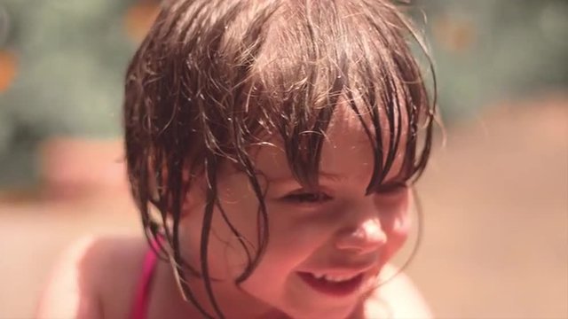 Close up of a cute little girl with wet hair playing outside and smiling
