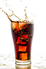 Ice cube droped in cola glass and cola splashing