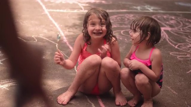 Two cute little girls being sprayed with a hose and running away
