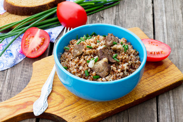Buckwheat with meat and tomatoes on a wooden background