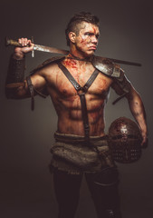 Muscular shirtless gladiator holding helmet and sword.