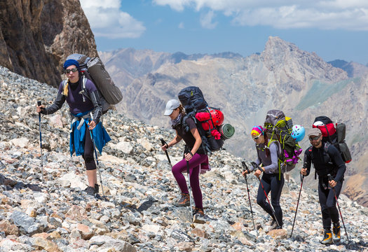 Group of Mountaineer Walking on Deserted Rocky Terrain Five Members Team Sport Clothing Going Heavy Load Backpacks Climbing Gear Up  Mountain Peaks Blue Sky Majestic Summits Shining Sun Background