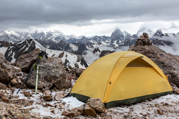 Yellow tent on mountain landscape Small Alpine camping Tent located on rocky terrain stone surface and high mountain hills and peaks on background evening sun light