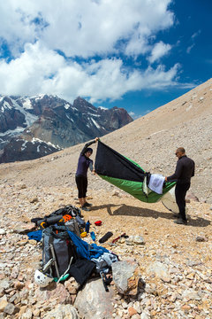 People Assembling Bivouac Group of Alpine Climbers Working on setting up Camping Tents with Many Gear Dropped Around and Rocky Mountain Moraine on Background