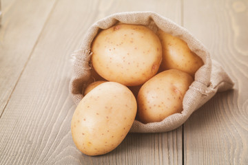 Fototapeta na wymiar organic raw potato in sack bag on wood table