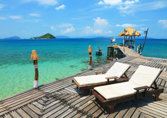 Sun beds on a wooden bridge in the sea with a ship and tropical islands
