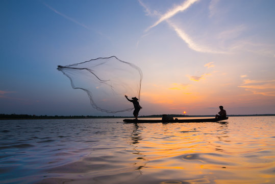 Silhouette of a fisherman throwing his net with sunset. Stock