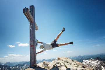 Man Clinging to Mountain Summit Cross on Windy Day
