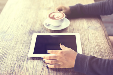 Girl hands with digital tablet and cappuccino on a wooden table,