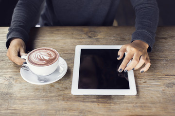 Girl hands with digital tablet and cup of coffee on a wooden tab