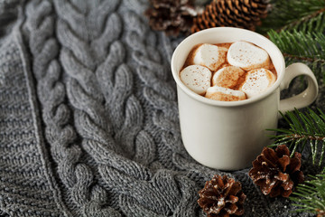 White cup of fresh hot cocoa or hot chocolate with marshmallows on knitted background, copy space for text