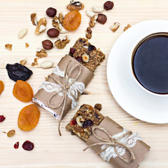 Obraz na płótnie Canvas Homemade rustic granola bars with dried fruits and handmade packaged and cup of coffee on wooden background