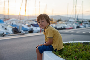 Sweet little child, toddler boy, sitting and watching the harbor