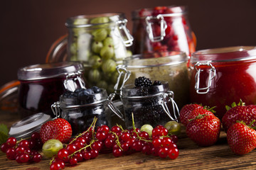 Jams in glass jars with wood and fresh berries 