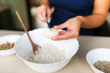 Young woman breaks the egg in the dough
