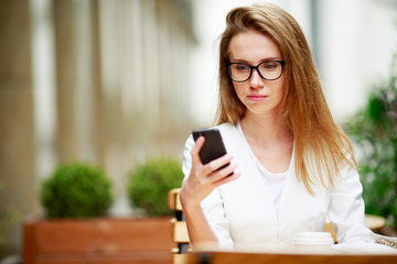 Girl texting on the smart phone in a restaurant terrace with an