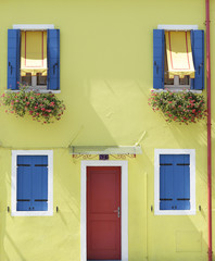Yellow painted wall with several windows with blue wooden shutters and awning, at the island of Burano, Venice, Italy