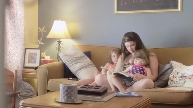 A mother reads a book to her daughters on the couch
