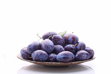 purple plums in a metal bowl on a white background