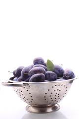 purple plums in a metal bowl on a white background